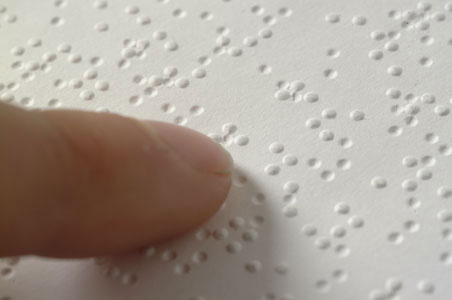 Imagem de uma folha escrita em Braille sendo lida